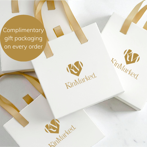 a collection of white gift bags with gold ribbons, each carrying a gold logo. The bags appear to be part of a gift packaging service, as indicated by the text "complementary gift packaging on every order" and "KinMarked".
