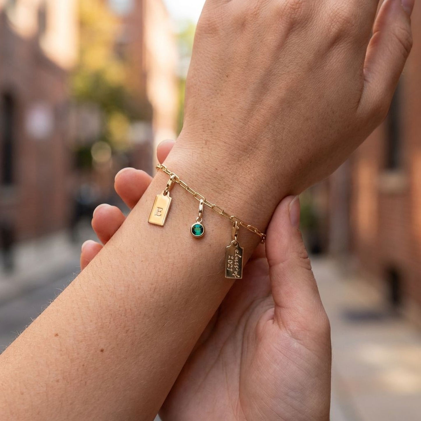A person's wrist wearing a gold bracelet with charms and a small green gemstone.