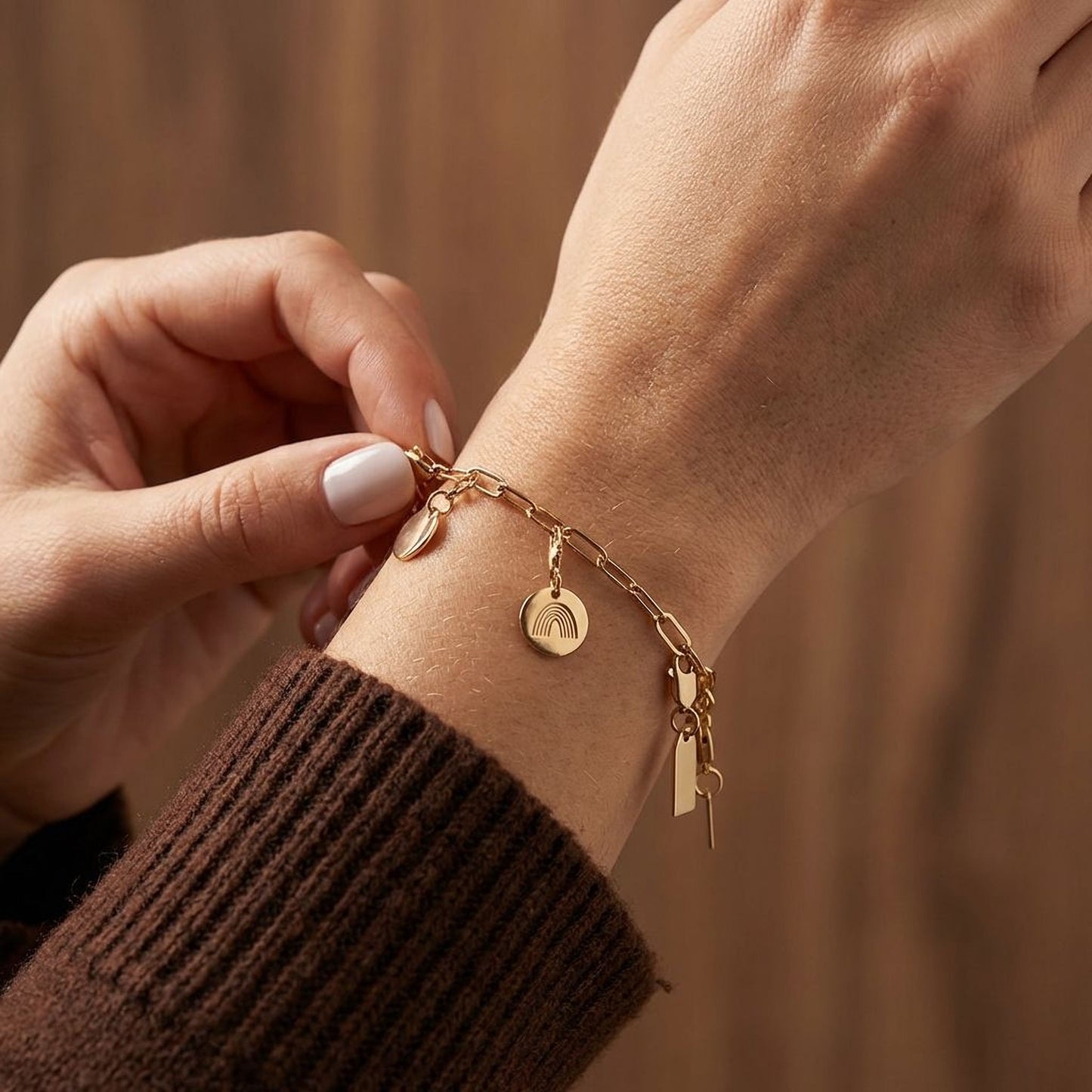 A person's hand wearing a gold-colored bracelet with charms on it.